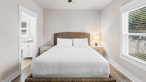 A bedroom with a large bed, a ceiling fan, a nightstand with a lamp, a window with blinds, and a door leading to a bathroom. - 30A Beach House - Beach Bayou (Santa Rosa Beach)