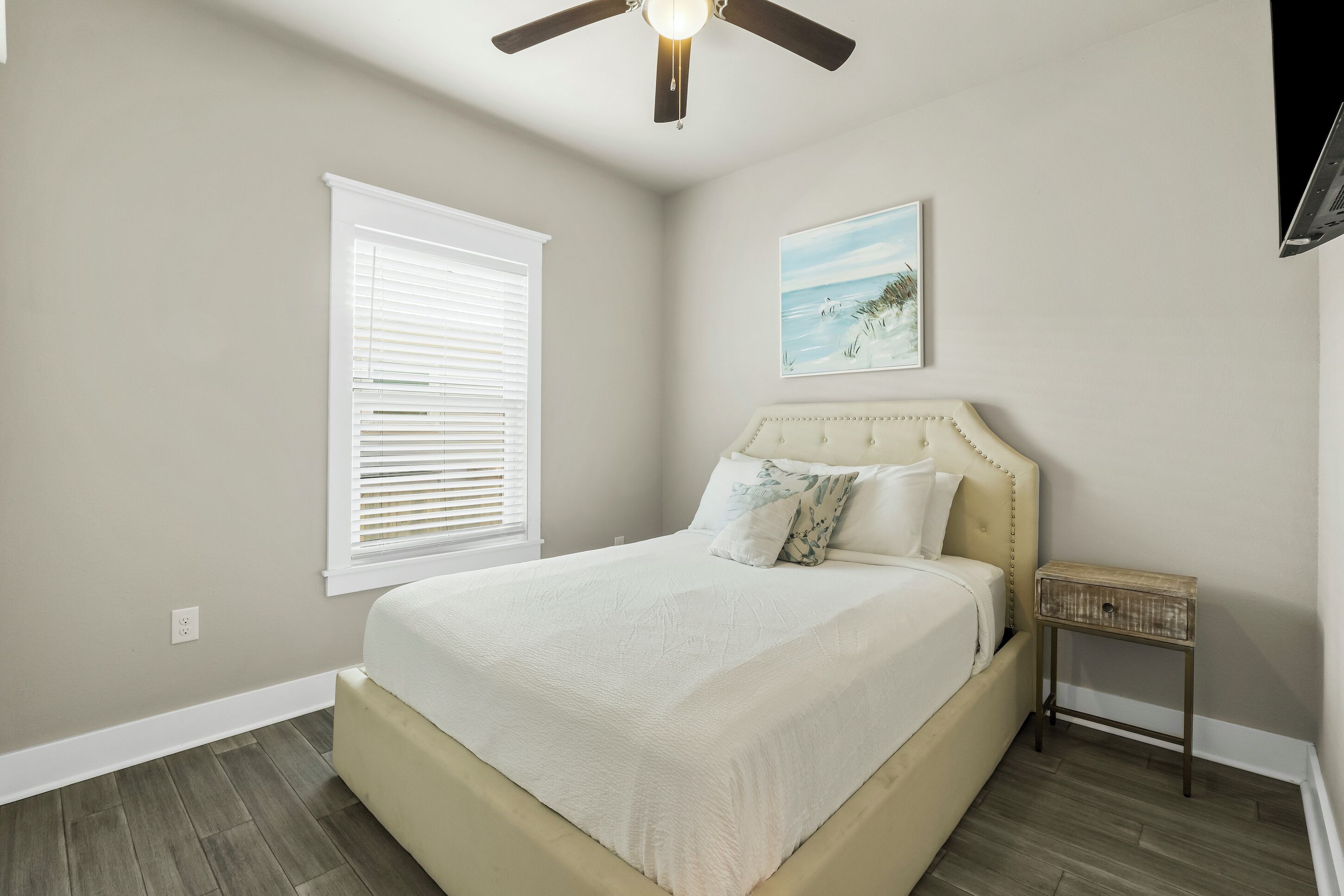 A bedroom with a bed, a ceiling fan, a nightstand, and a window with blinds.