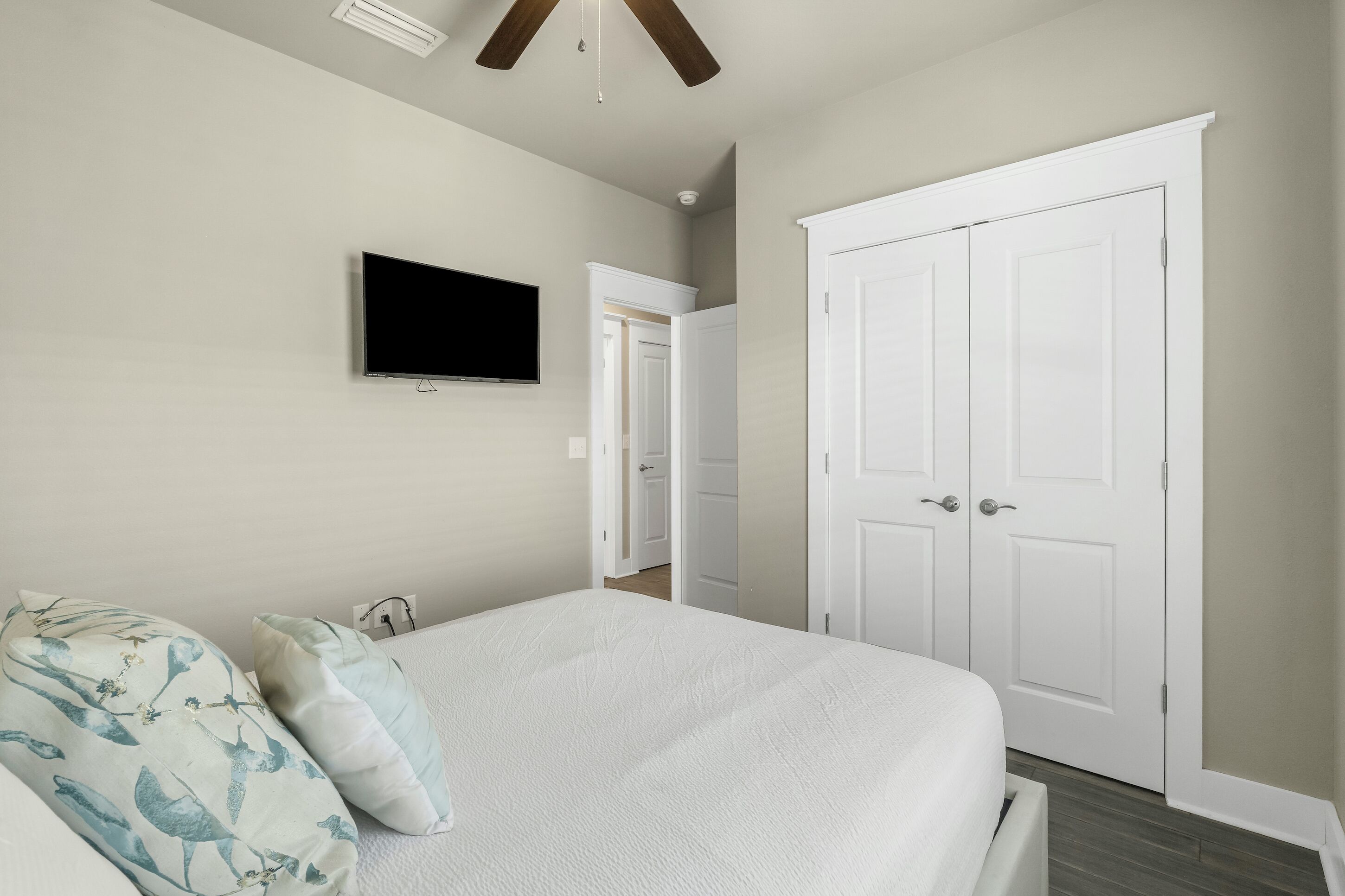 A bedroom with a bed, a TV mounted on the wall, and a white wardrobe.