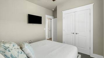 A bedroom with a bed, a TV mounted on the wall, and a white wardrobe.