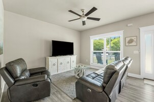 A living room with a flat-screen TV, leather recliners, a glass coffee table, and a ceiling fan.