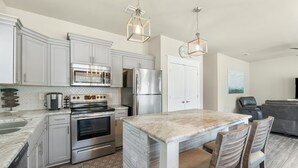 A modern kitchen with stainless steel appliances, a marble island, and pendant lighting. - 30A Beach House - Beach Bayou (Santa Rosa Beach)