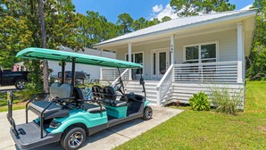 A golf cart parked in front of a house with a porch and a staircase leading to the entrance. - 30A Beach House - Beach Bayou (Santa Rosa Beach)