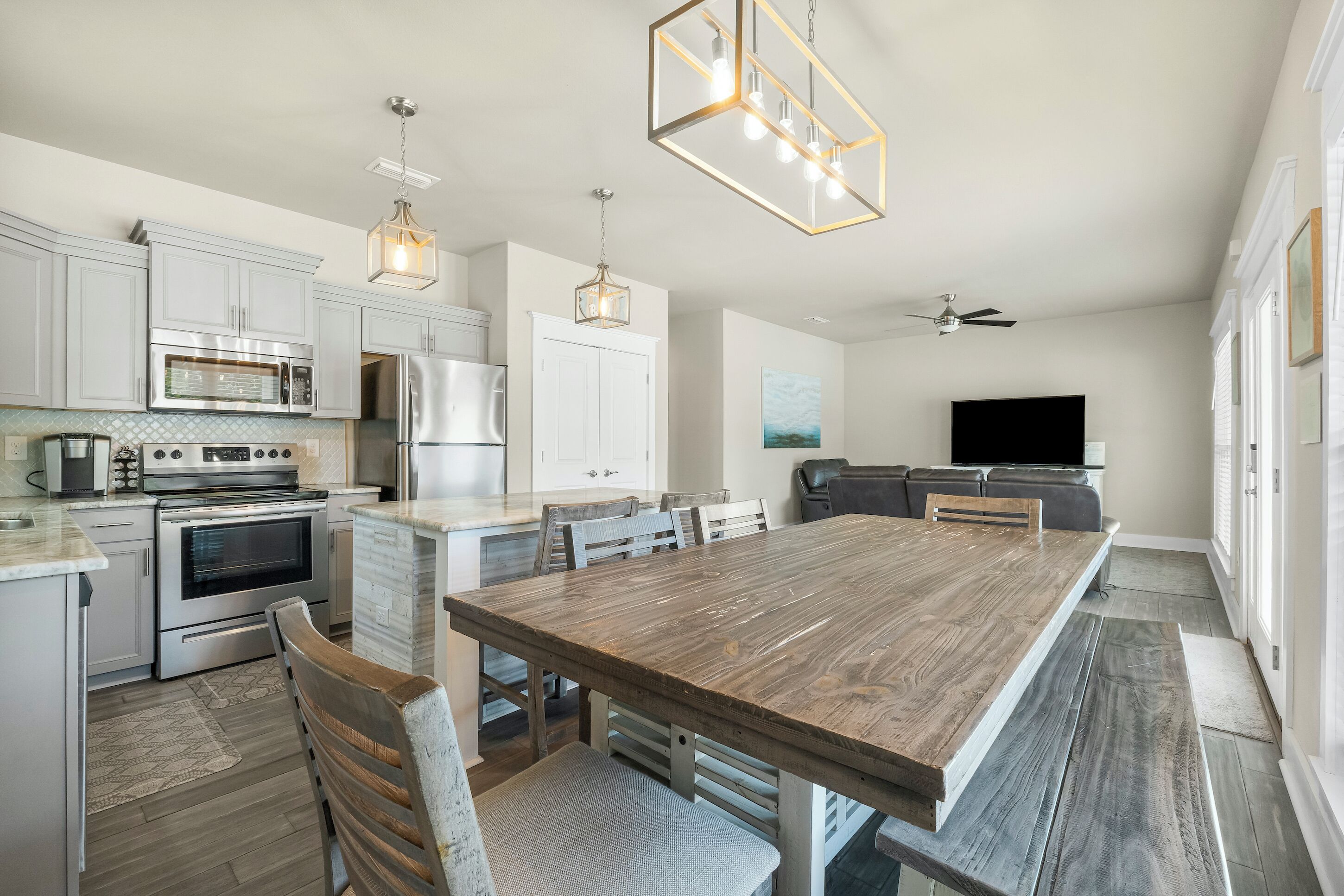 A modern kitchen with white cabinetry, stainless steel appliances, and a large wooden dining table.