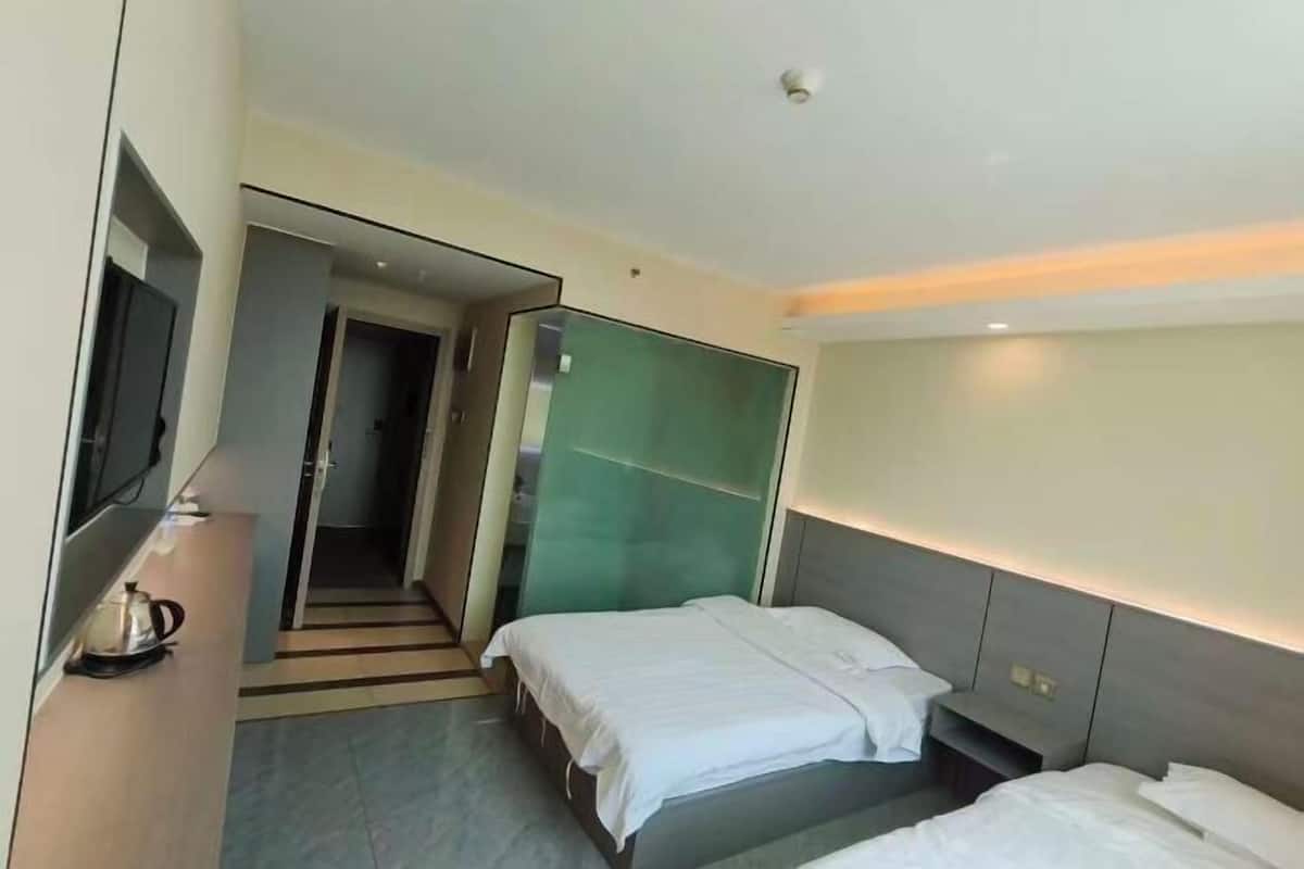 A hotel room with two beds, a TV, a mirror, and a door leading to a hallway.