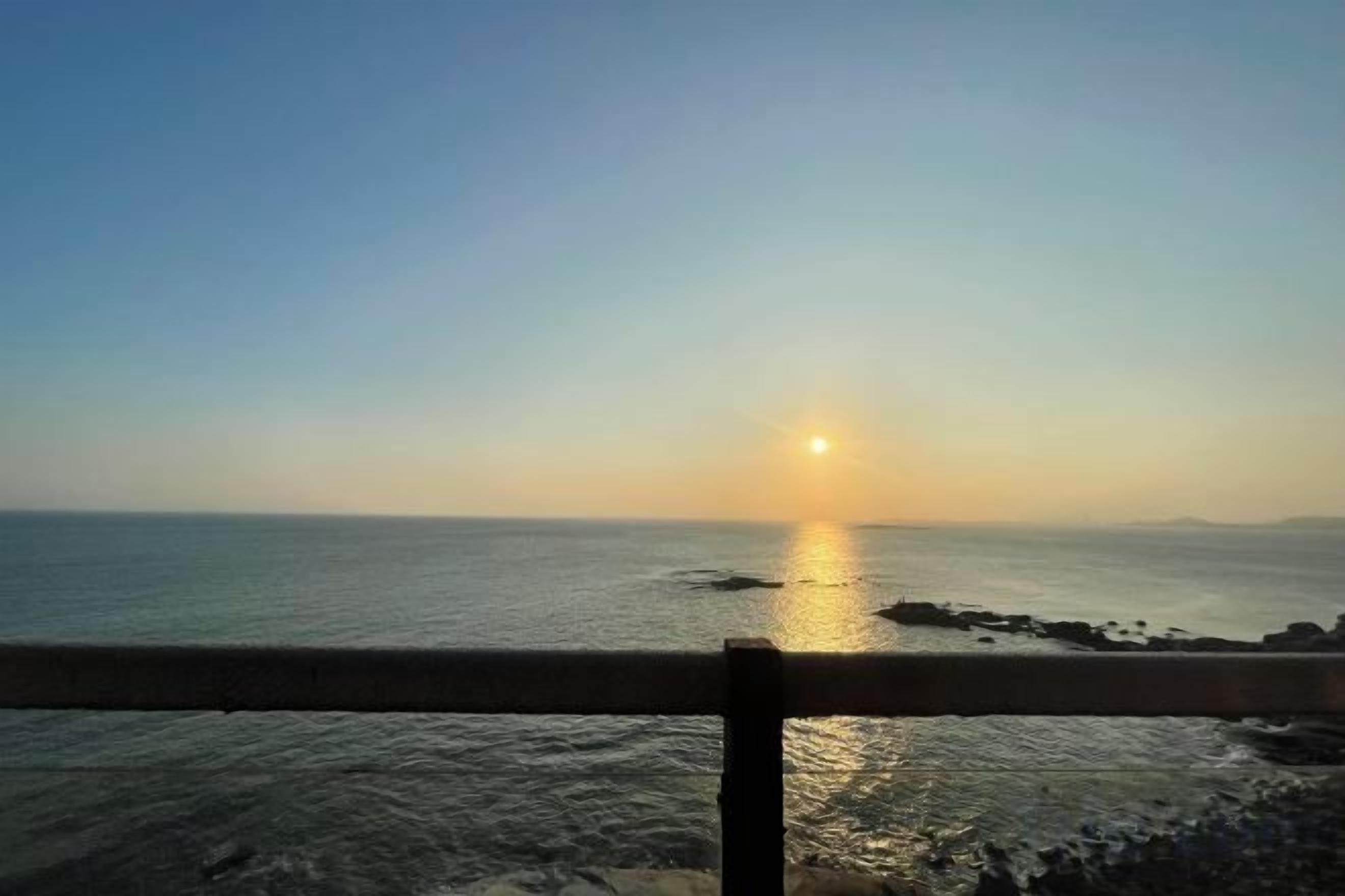 A sunset over the ocean with a railing in the foreground.