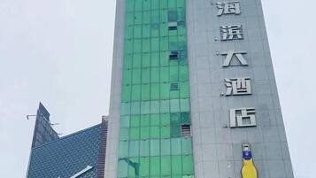 A tall building with a green facade and a large yellow bottle logo.