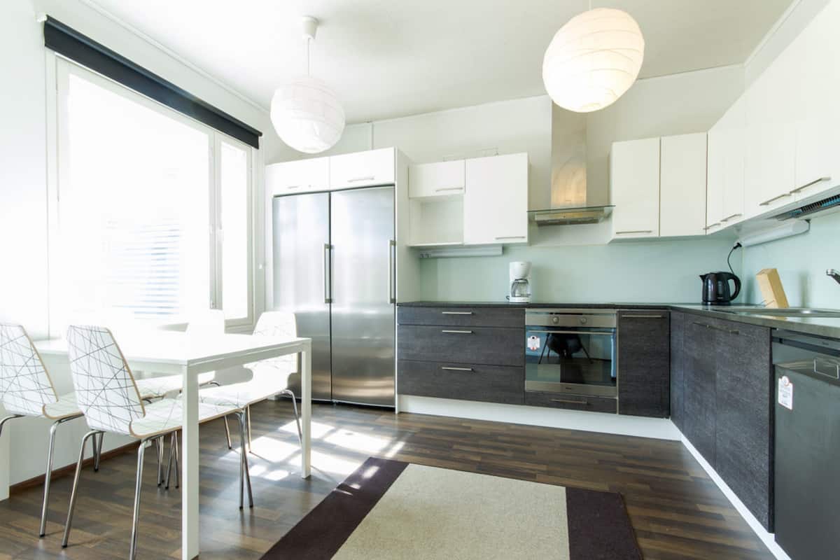 A modern kitchen with white cabinets, stainless steel appliances, and a dining area with a white table and chairs.