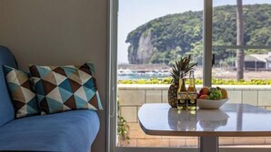 Une pièce avec vue sur une falaise, une table avec des bouteilles et des fruits, et un canapé bleu agrémenté de coussins à motifs.