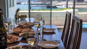 Une table à manger dressée avec des assiettes, des verres et une bouteille, donnant sur un paysage aquatique pittoresque.