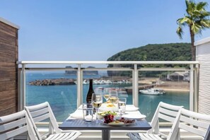 A balcony with a table set for dining, overlooking a coastal area with boats and a forested hill. - Daikyo Engtsuto Villa (Shirahama)