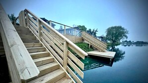 Een houten terras met een trap naar een steiger boven kalm water.