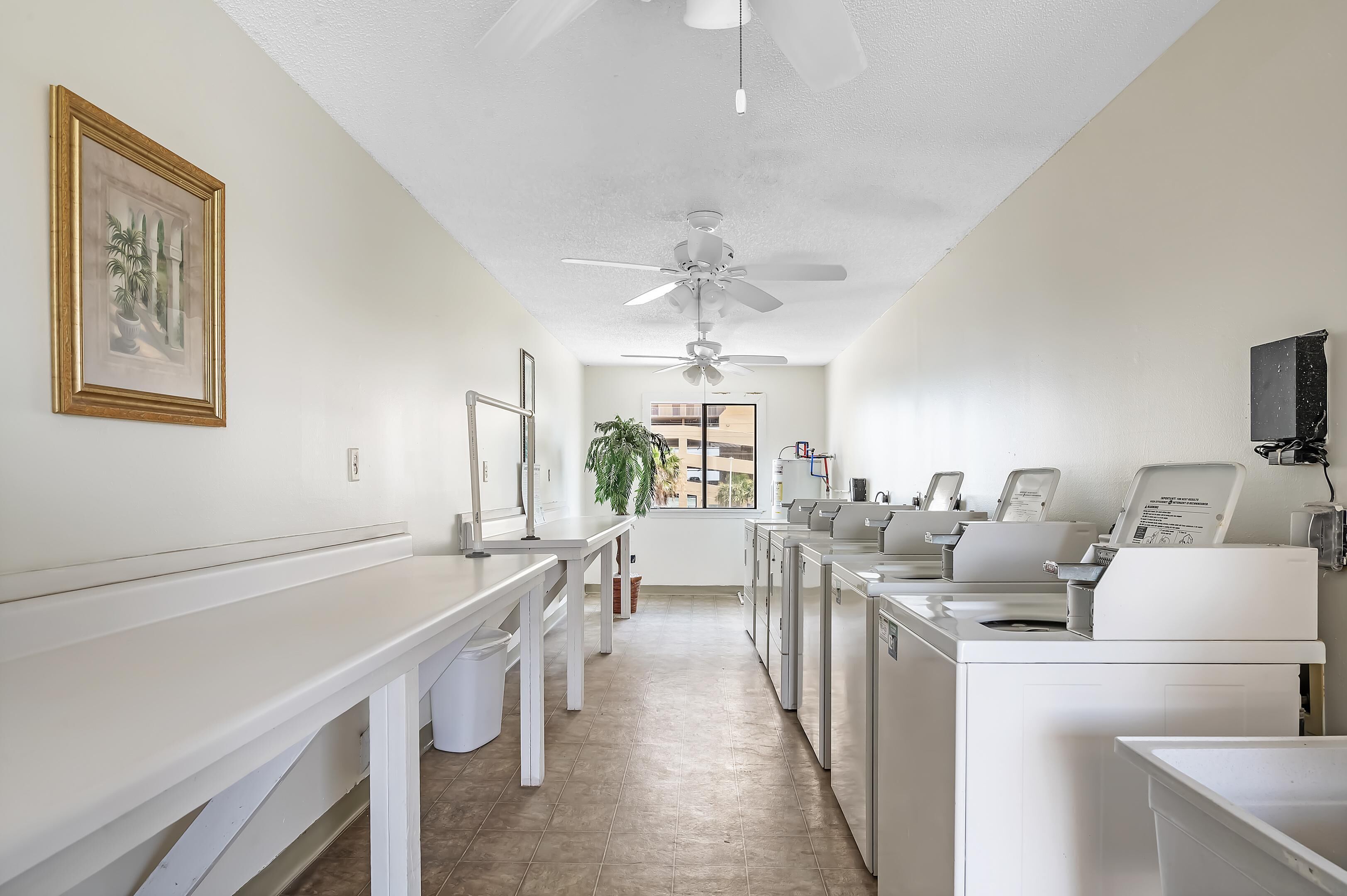 A laundry room with white appliances, a ceiling fan, and a framed picture on the wall.