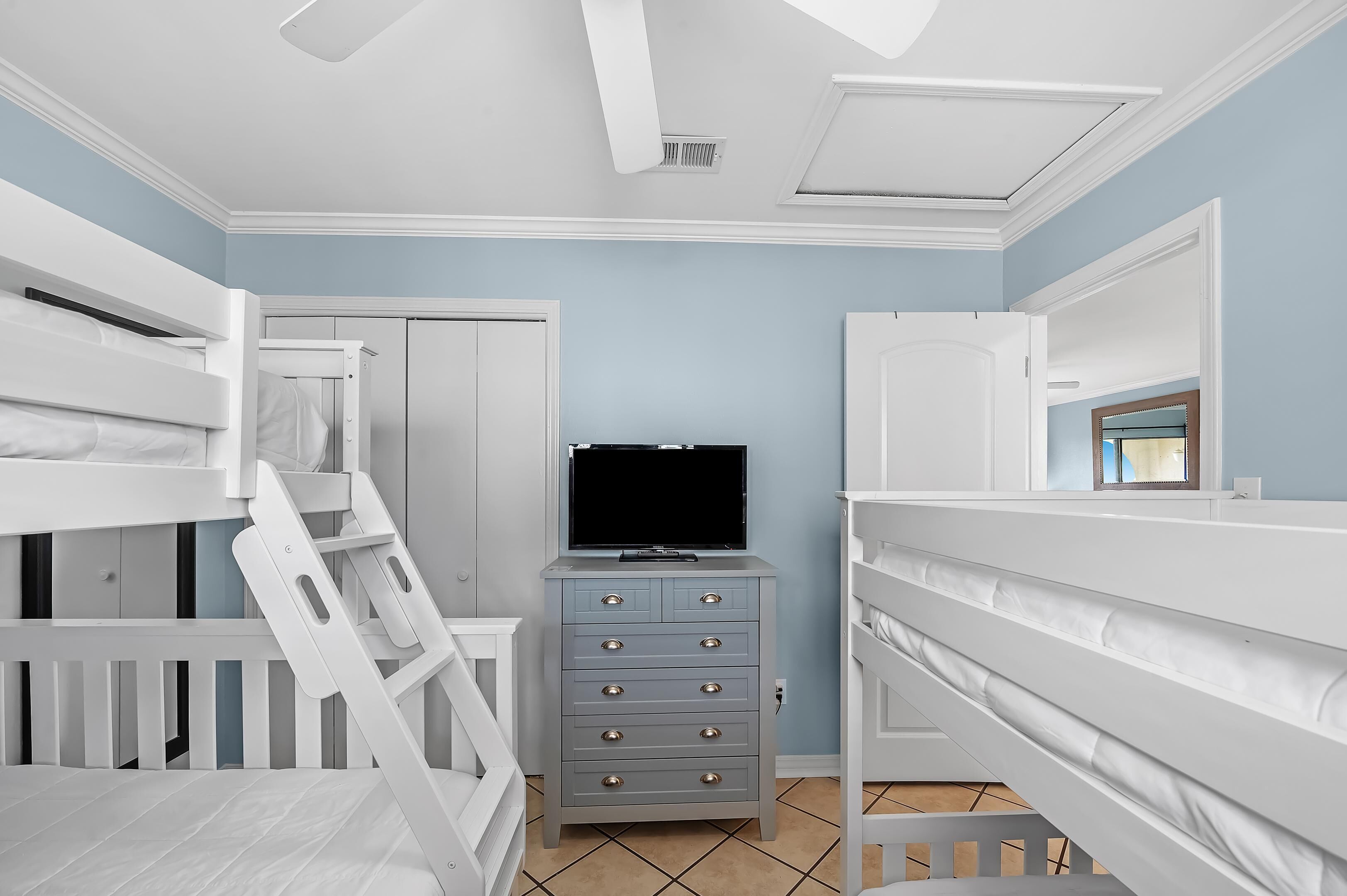 A child's bedroom with bunk beds, a dresser, and a television.