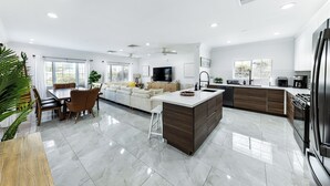 A modern kitchen with a central island, built-in appliances, and a dining area with a sofa and chairs. - Beautiful Tropical Villa with Private Pool / Pool Bar /Grill / Sandy Beach (Nassau)