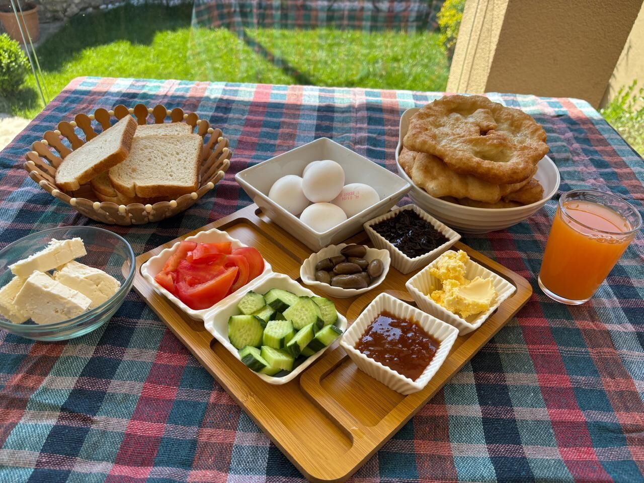 A picnic setup with bread, eggs, fruit, and condiments on a checkered tablecloth.