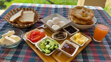 A picnic setup with bread, eggs, fruit, and condiments on a checkered tablecloth.