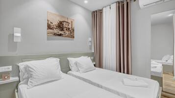 Una camera d'albergo con due letti singoli, un condizionatore d'aria a parete, uno specchio e un quadro raffigurante una scena di strada.