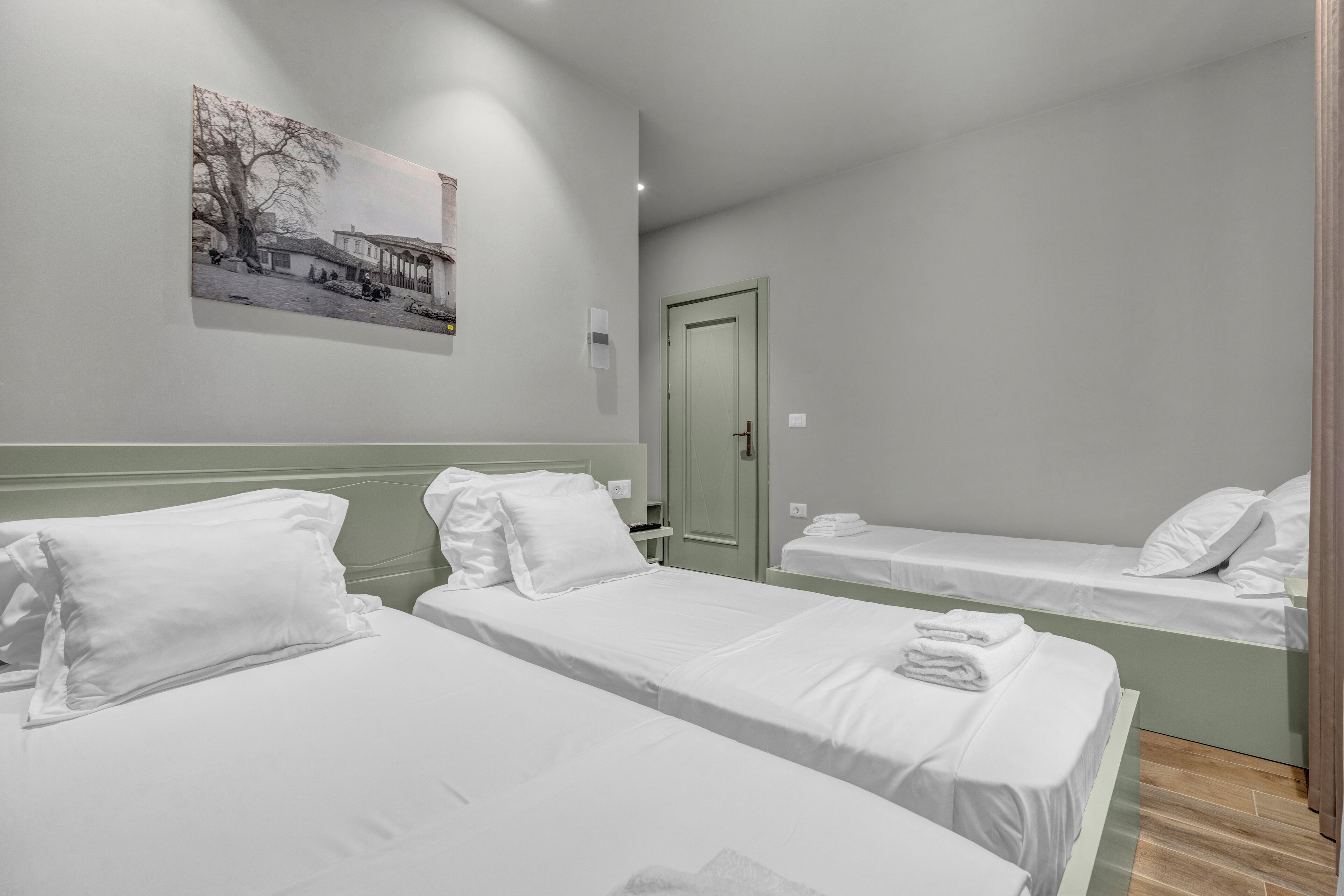 A hotel room with two single beds, a green door, and a wall-mounted picture.