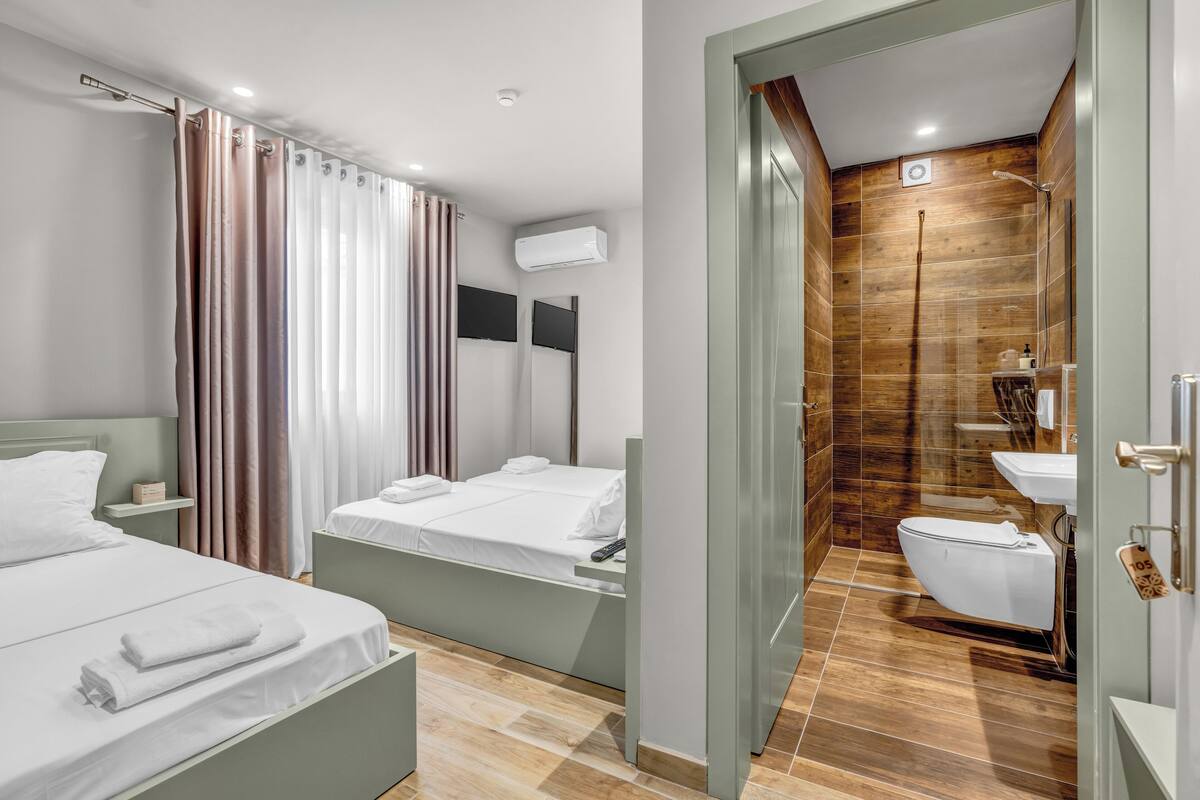 Une chambre d’hôtel avec deux lits, un espace douche, un lavabo et un téléviseur à écran plat.
