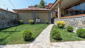 Une maison aux murs de pierre, avec un toit en tuiles, un chemin pavé et de petits arbustes.
