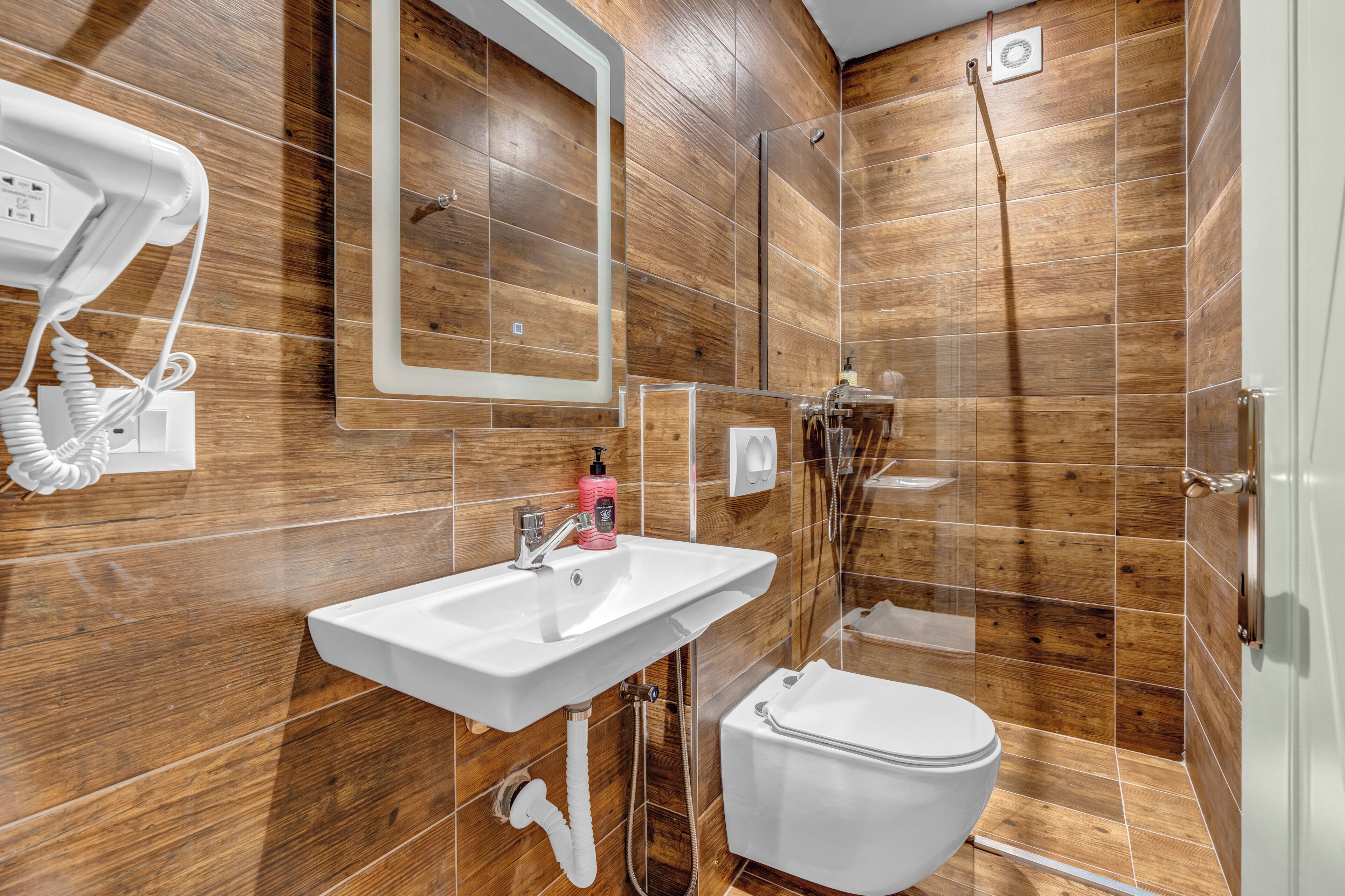 A bathroom with wooden walls, a white sink, a mirror, a hairdryer, and a shower.