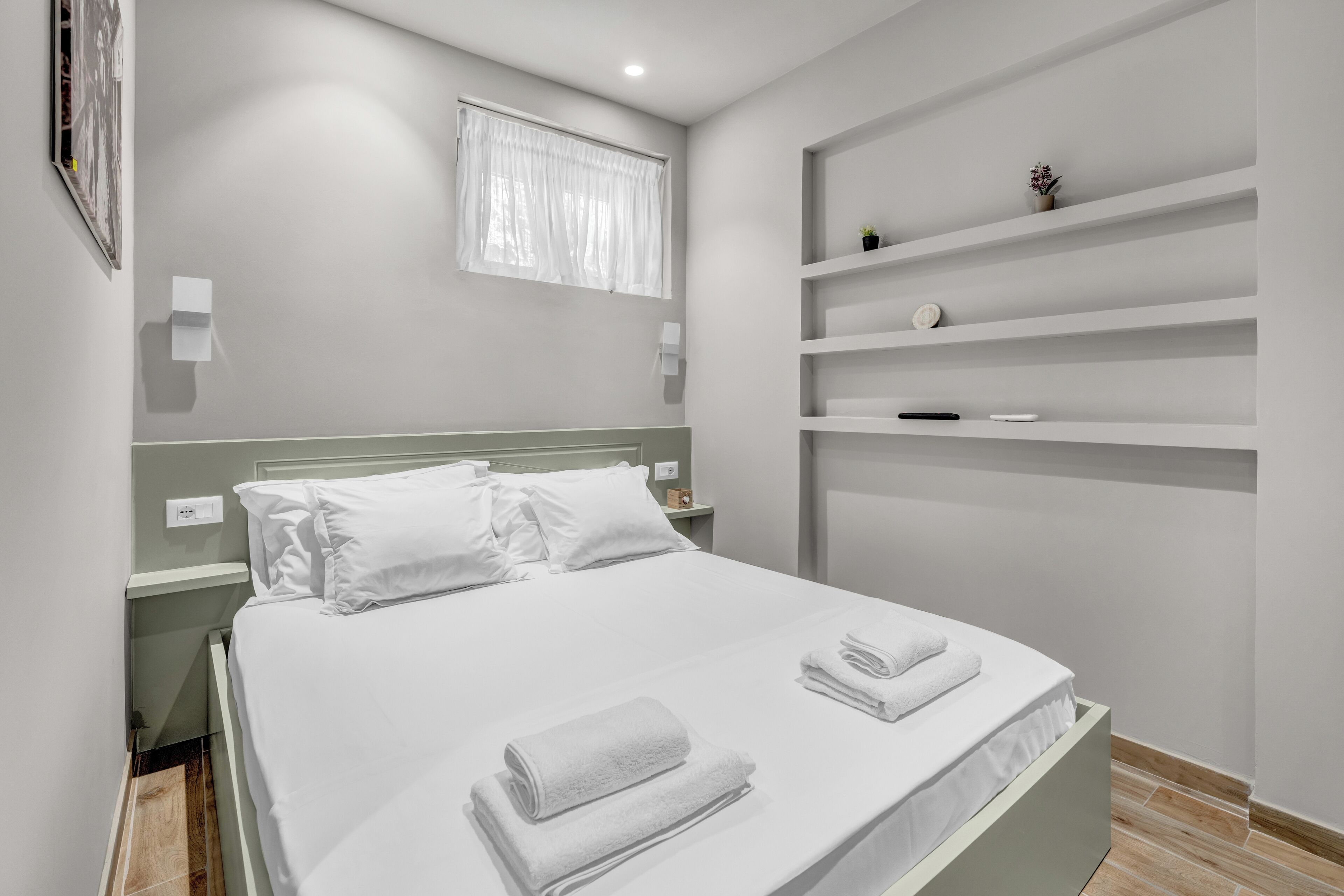 Une chambre d’hôtel moderne avec un lit bien fait, une table de chevet, une étagère avec des objets décoratifs et une fenêtre avec des rideaux.