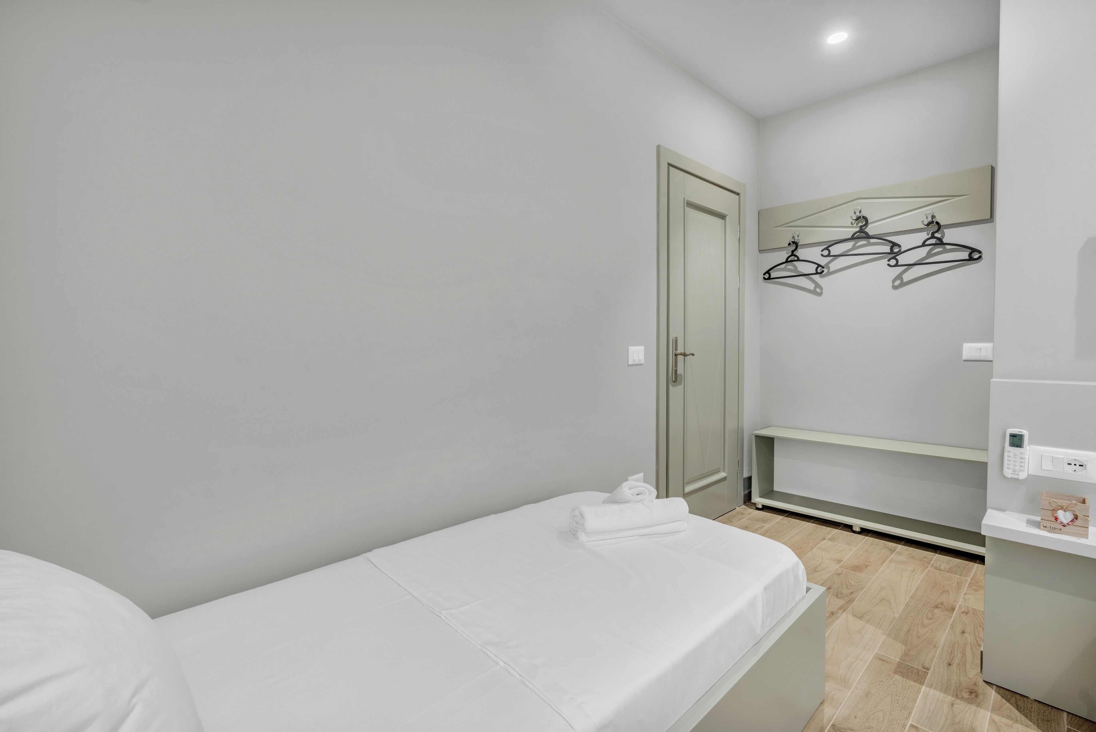 Een moderne hotelkamer met een enkel bed, een kledingkast, een spiegel met kapstok en een klein plankje met een telefoon en een decoratief object.
