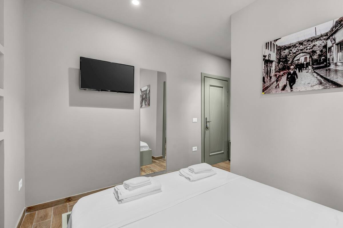 Une chambre d’hôtel moderne avec un téléviseur à écran plat fixé au mur, un tableau représentant une scène de rue et des serviettes soigneusement pliées sur le lit.