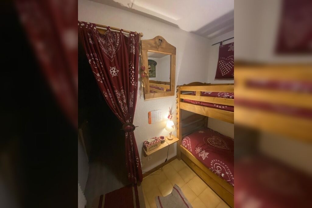 A small, cozy room with a bunk bed, a mirror, a bedside table with a lamp, and a curtain.