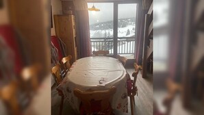 A dining area with a round table and chairs, a view of a snowy landscape through large windows, and a wooden cabinet to the left. - Apartment Les Saisies (Hauteluce)