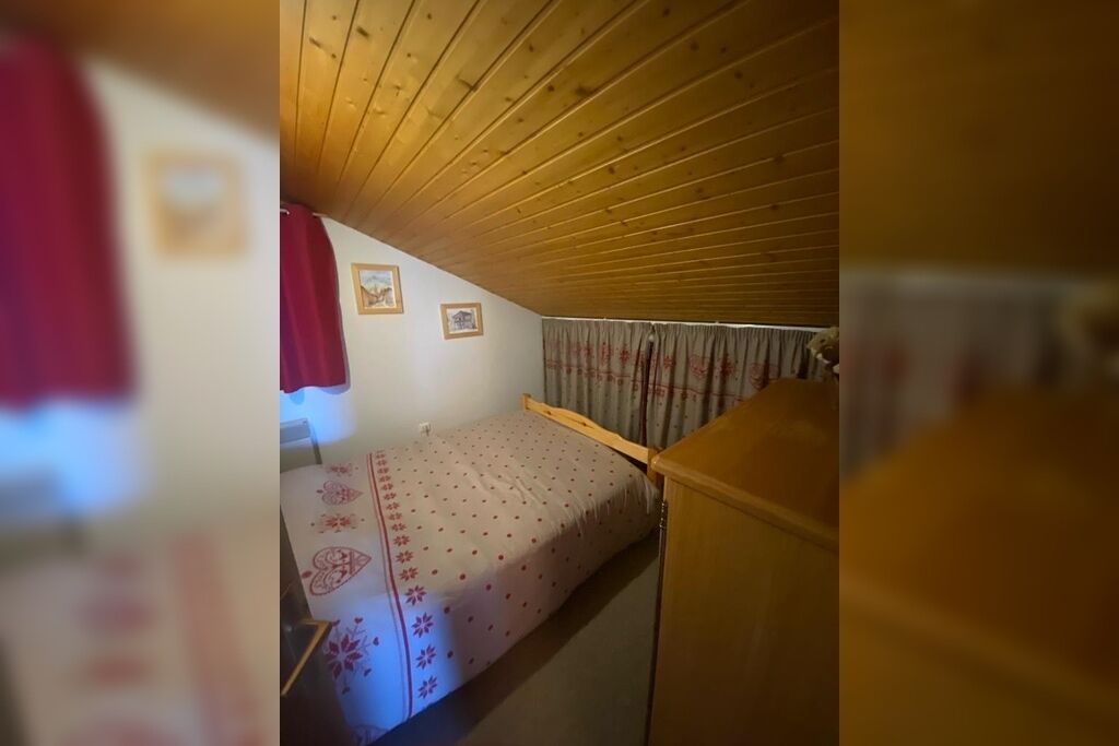 Een kleine, smalle kamer met een houten plafond en een enkel bed met een beddegoed met een patroon.