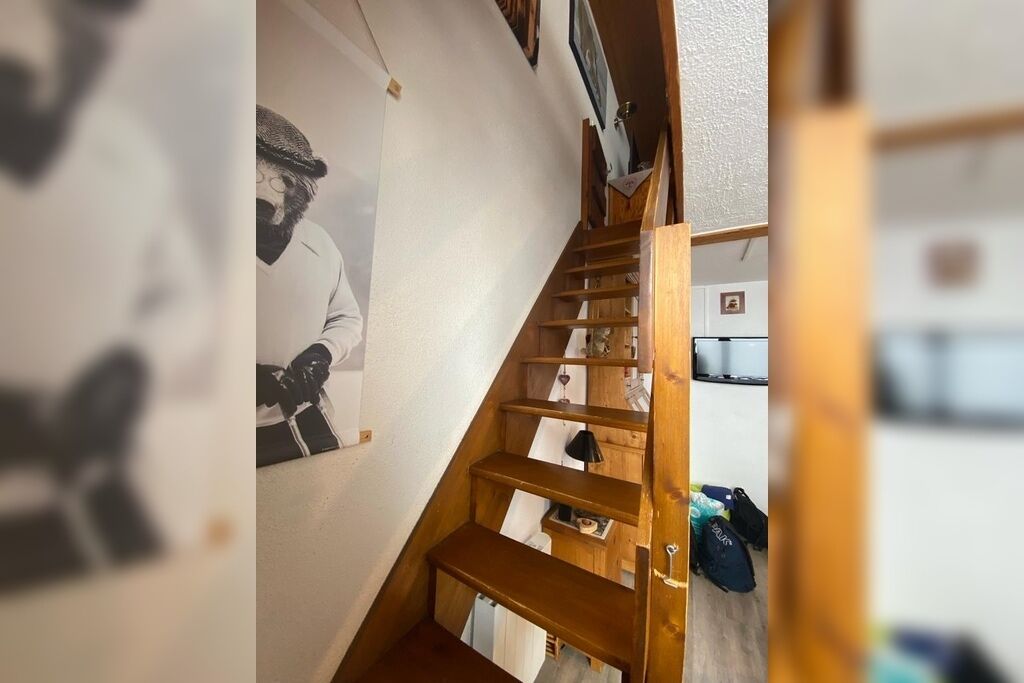 A wooden staircase with a handrail, leading to a landing with a small table and a chair.