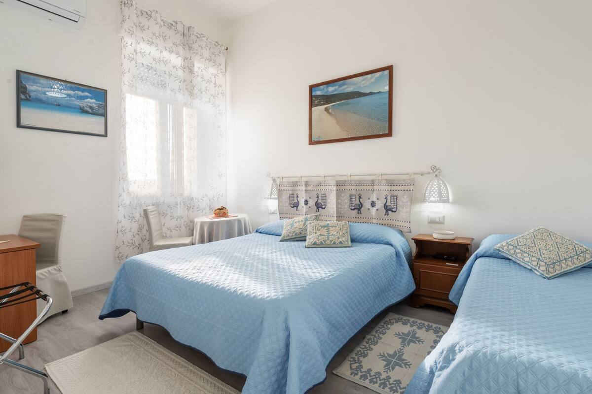 Ein Schlafzimmer mit zwei Betten, einem kleinen Tisch, einem Stuhl und einem Fenster mit Vorhängen.