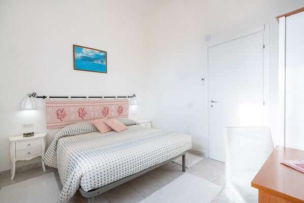 A bedroom with a bed, bedside tables, a chair, a desk, a picture on the wall, and a door.
