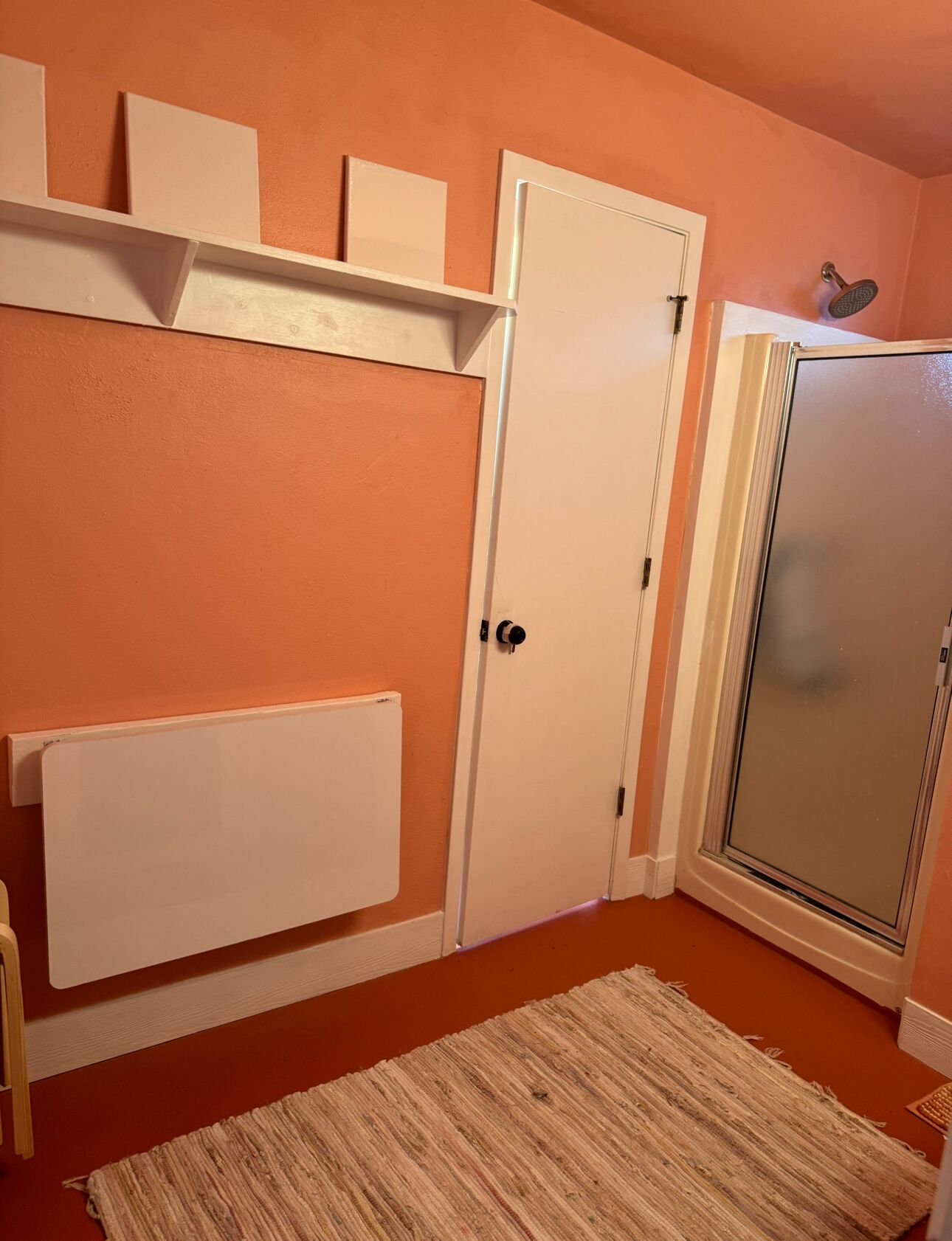 Un baño con un radiador blanco, cabina de ducha y un tapete beige.