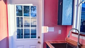A compact kitchen with a white door, a built-in sink, and a dark cabinet above the counter. - Vibey & Chill Pool House- Pool, Slide & Hot Tub! Outdoor Bar! Events/Parties! (College Station)