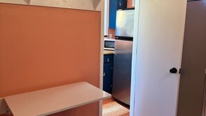 A compact kitchen with a white refrigerator, a blue cabinet, and a white shelf unit. - Vibey & Chill Pool House- Pool, Slide & Hot Tub! Outdoor Bar! Events/Parties! (College Station)