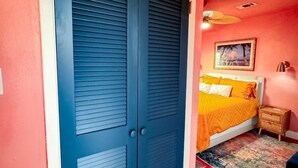 A bedroom with a double door, a bed with orange bedding, a nightstand, and a ceiling fan. - Vibey & Chill Pool House- Pool, Slide & Hot Tub! Outdoor Bar! Events/Parties! (College Station)