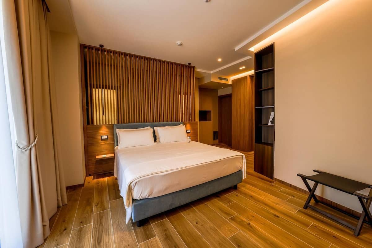 A modern hotel room with a large bed, wooden paneling, and a built-in bench.