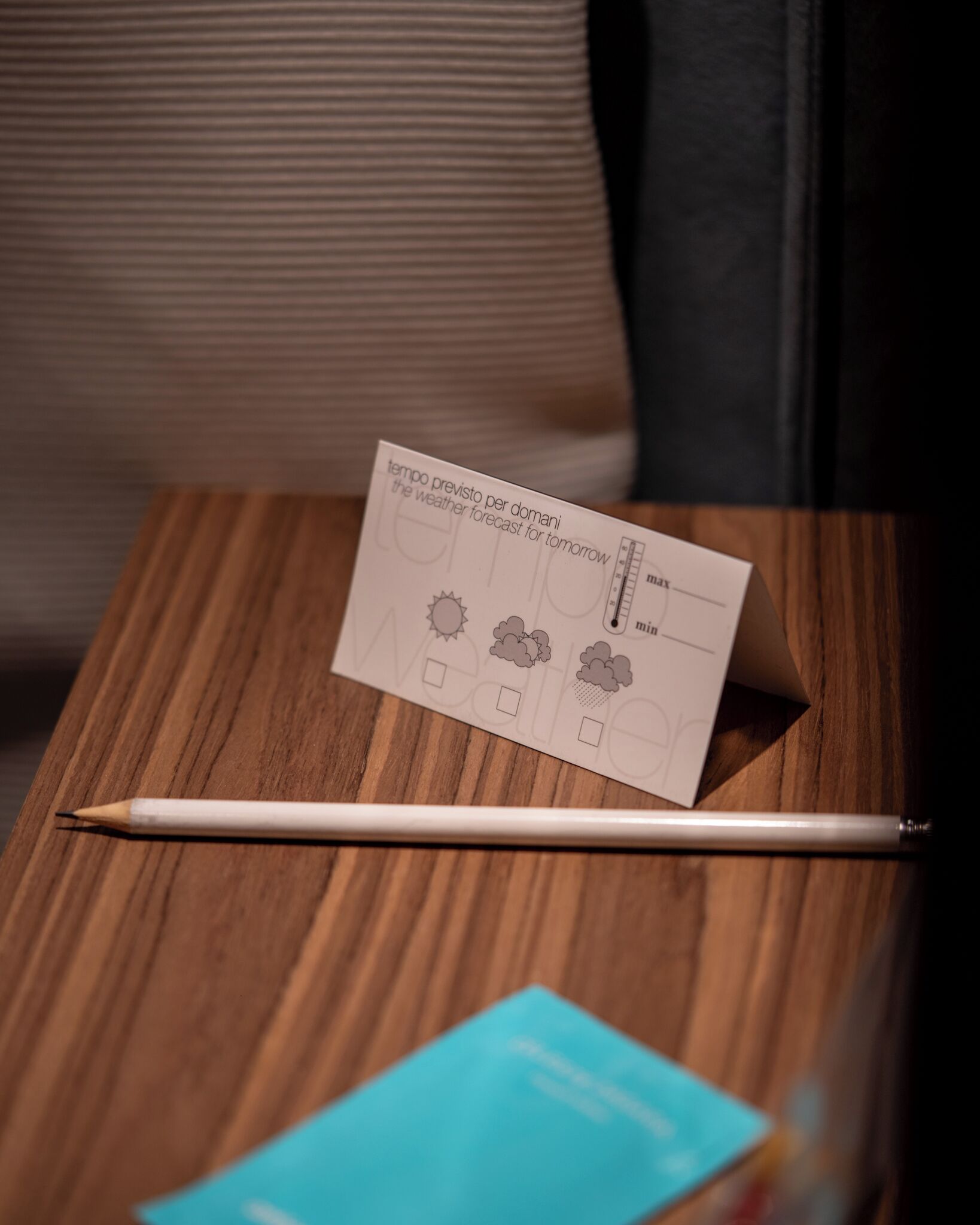 A weather forecast card on a wooden table with a pencil and a blue card.
