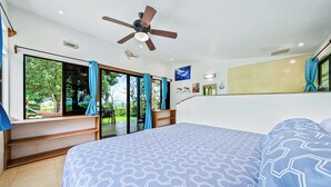 Une chambre dotée d’un grand lit, d’un ventilateur de plafond, d’une vue sur l’extérieur et d’une porte-fenêtre coulissante.