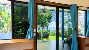 Une pièce dotée d’une porte-fenêtre coulissante donnant sur une terrasse avec une table et des chaises, un ventilateur de plafond et une vue sur la verdure et les arbres.