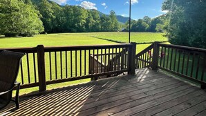 A wooden deck with a red canopy, overlooking a green field and a mountain range.