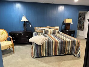 A bedroom with a bed, two nightstands, a chair, a dresser, and a door with a painting.