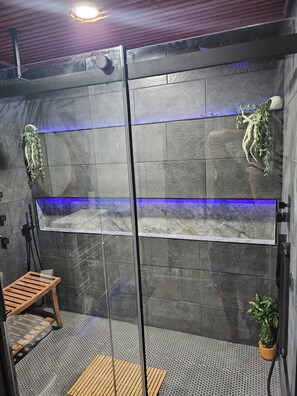 A modern shower area with stone walls, a wooden bench, and a potted plant.