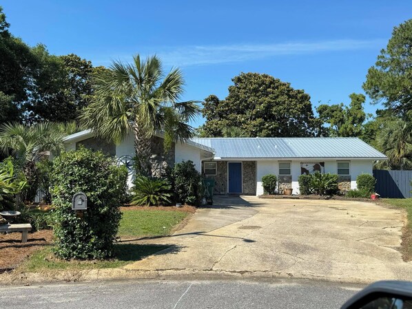 A single-story house with a blue metal roof, a front porch, and a driveway leading to the front door.