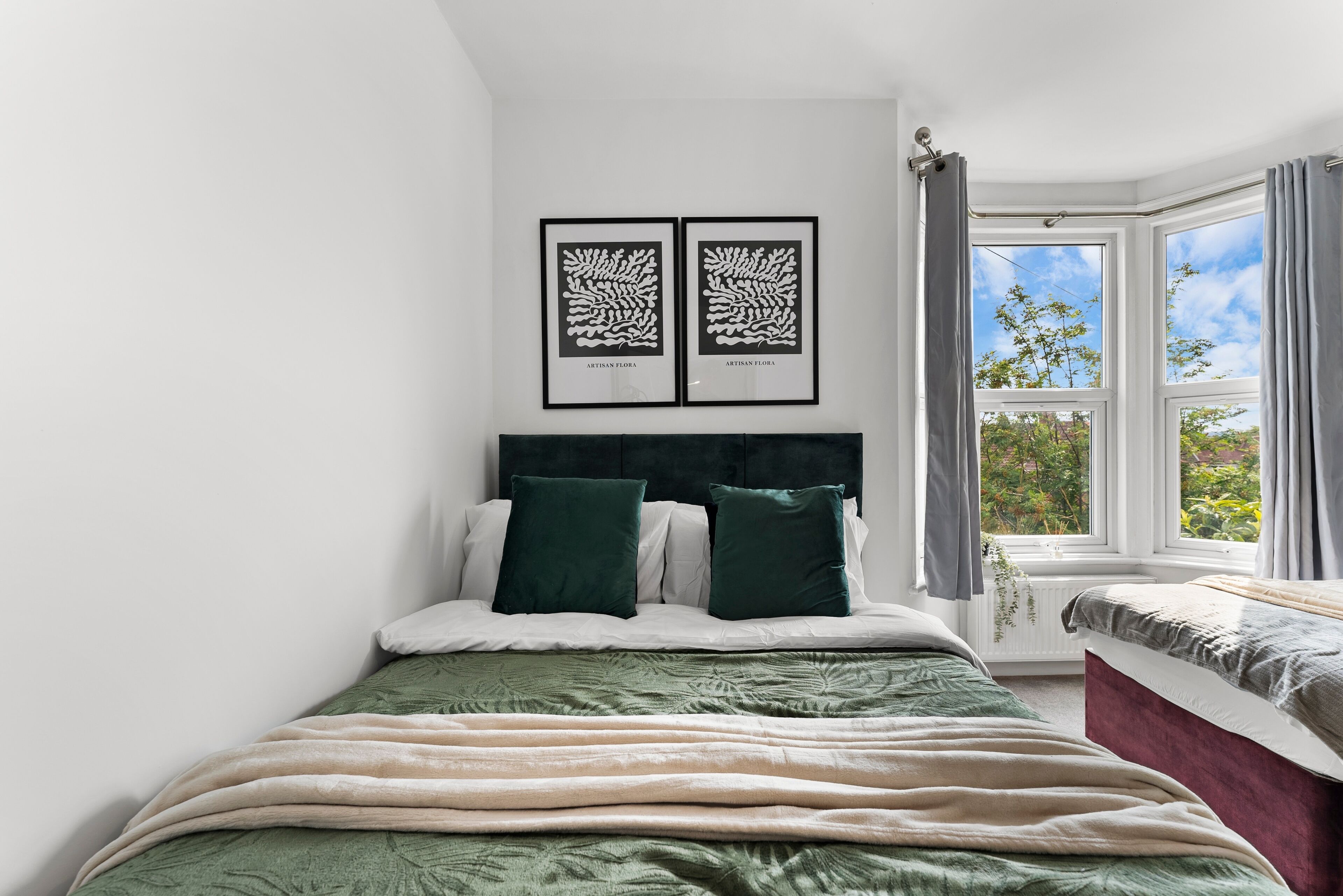 Un dormitorio con cama, dos obras de arte enmarcadas, una ventana con cortinas y vistas a la vegetación.