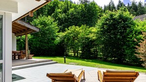 A patio with wooden loungers, a covered seating area, and a view of a mountainous landscape. - Chalet Hammersbach (Grainau)