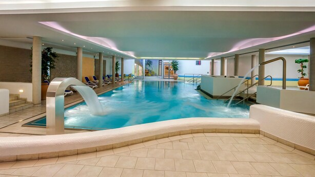 An indoor swimming pool with a water slide, lounge chairs, and a stone wall. - Chalet Hammersbach (Grainau)